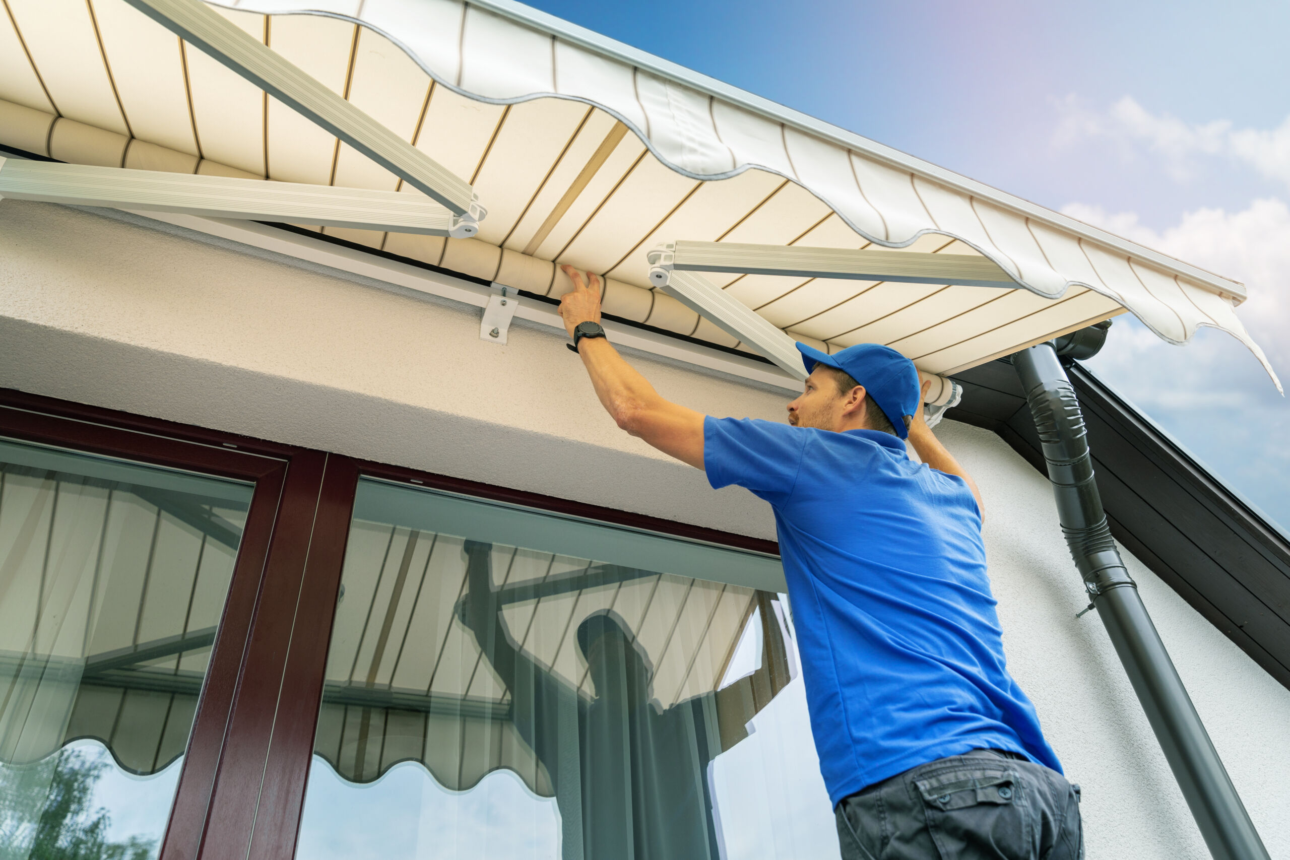 worker install an awning on the house wall over the terrace window Συστήματα Σκίασης